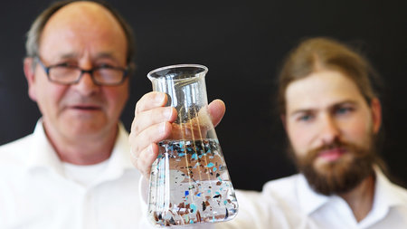 Zwei Forscher betrachten in einem Wasserglas Mikropartikel.