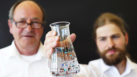 Two researchers observe microparticles floating in a glass of water.
