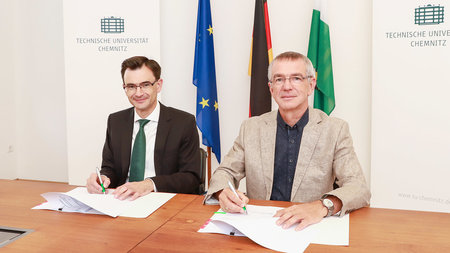 Prof. Dr. Gerd Strohmeier and Dr. Thomas Raschke sitting at a table and signing papers.