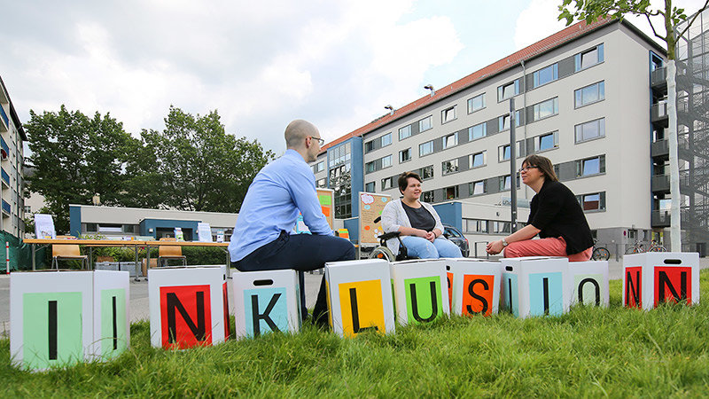 Three people sitting on cubes with letters that spell “inclusion”. 
