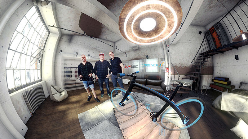 Drei Entwickler zeigen ein neues Bogenfarrad in einer virtuellen Präsentationsumgebung.