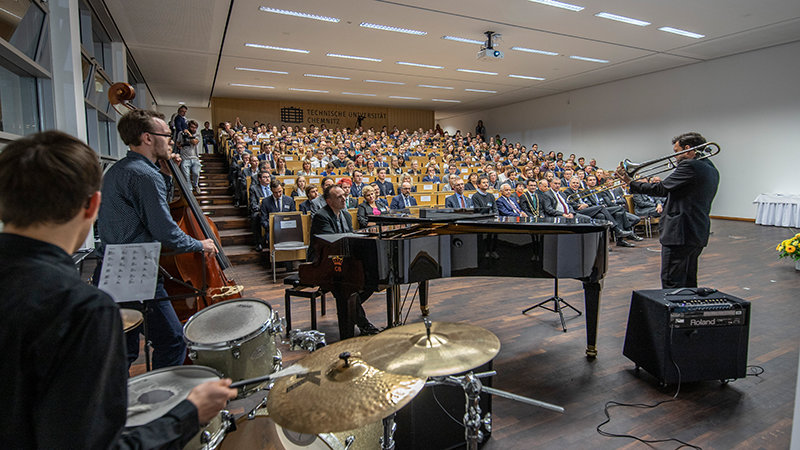 Vier Herren der BigBand spielen auf ihren Instrumenten, im Hintergrund das vollbesetzte Auditorium