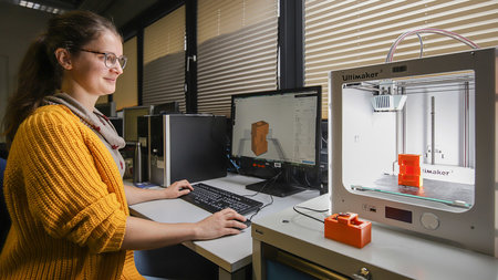 A young woman is working with a 3D printer.