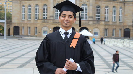 A young indian man in talar holds his diploma.