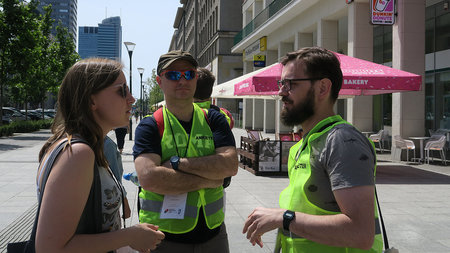 A young man with beard, glasses and a emergency vest interviews young people.