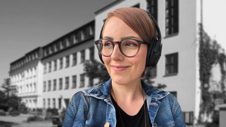 A smiling woman with short hair and glasses wearing headphones and a jeans jacket.