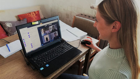 A woman uses a laptop computer. The computer screen displays video chat software with four participants.