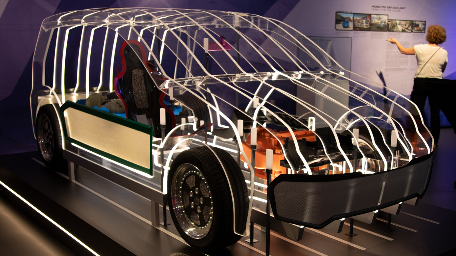 Gläserne Autokarosse steht in einem Ausstellungsraum.