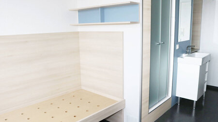 Photo of a single bed, small sink, and shower in the dormitory.