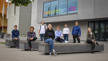 A group of eight people sit spread out among benches in front of the Weinholdbau at Chemnitz University of Technology