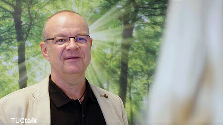 A man in glasses and a jacket stands in a forest.