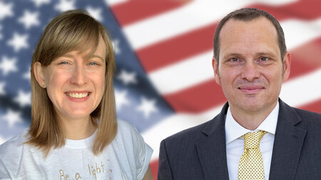 Ein junger Mann im Anzug und eine jugne Frau lächeln.