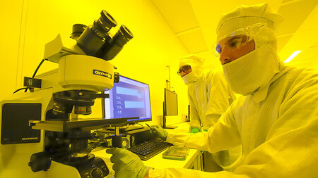 Photo of two researchers in protective gear with a microscope and a computer.