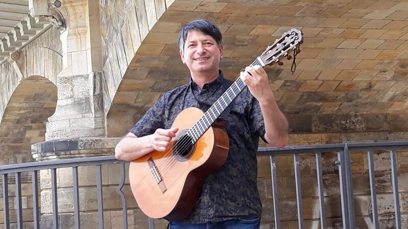 Mann mit Gitarre steht unter einer Brücke 