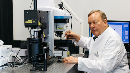 Photo of a man in a lab coat sitting before a microscope