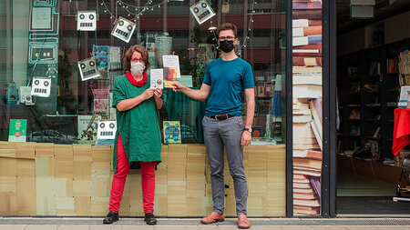 Eine FRau und ein Mann stehen vor dem Schaufenster einer Buchhandlung und halten Bücher in den Händen.