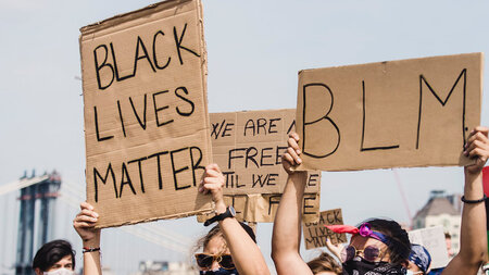 Photo of protestors holding up signs written on cardboard reading “Black Lives Matter” and “BLM.”