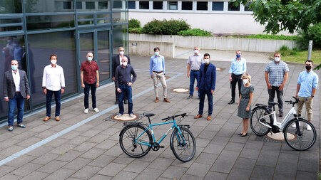 Mehrere Personen stehen vor einem Gebäude, im Vordergrund stehen zwei Fahrräder.