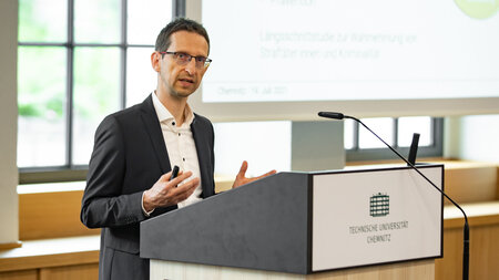 Mann im dunklen Anzug steht an einem Rednerpult.