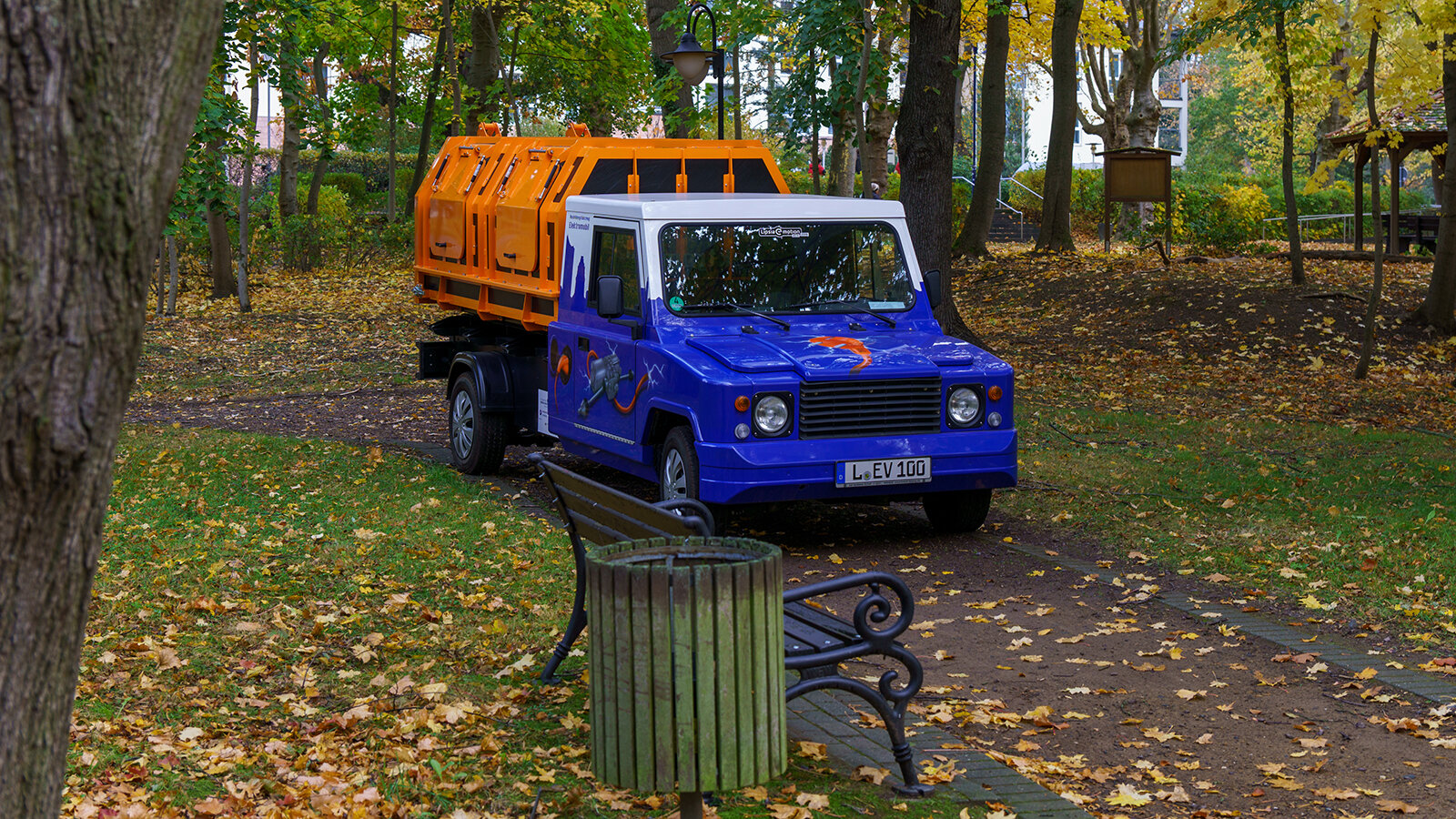 Ein Fahrzeug steht in einem Park vor einem Mülleimer.