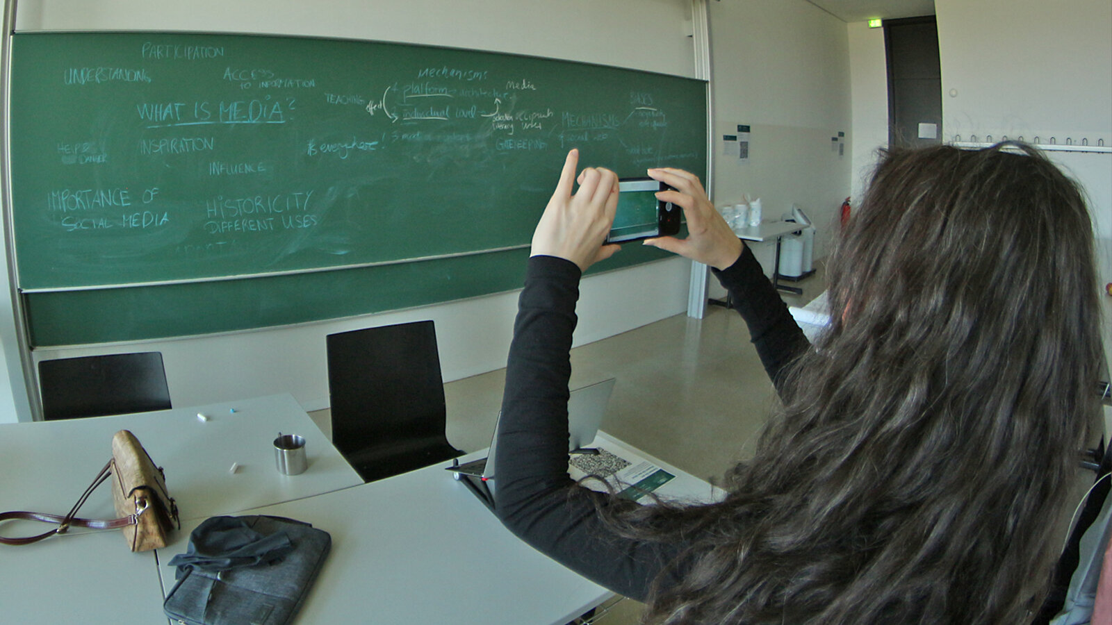A young woman takes a picture of a blackboard with her cell phone.