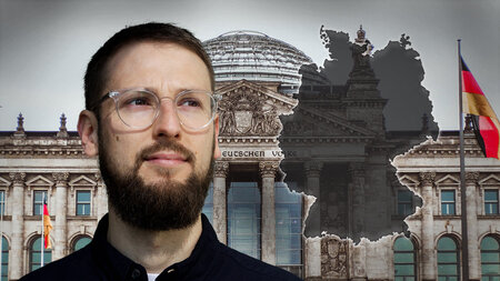 A young man with glasses and a beard stands in front of the Reichstag building and smiles.
