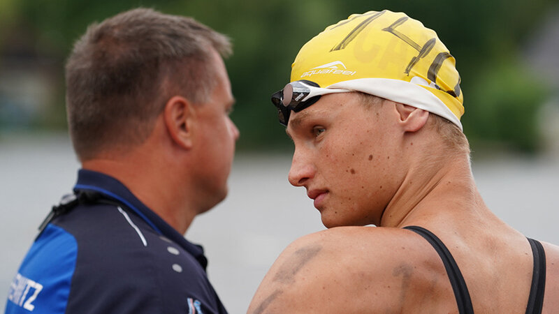 A man in a swimming cap standing next to a man in a tracksuit