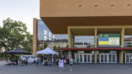 Zwei Pavillons und Sitzgruppen stehen vor einem großen Gebäude.