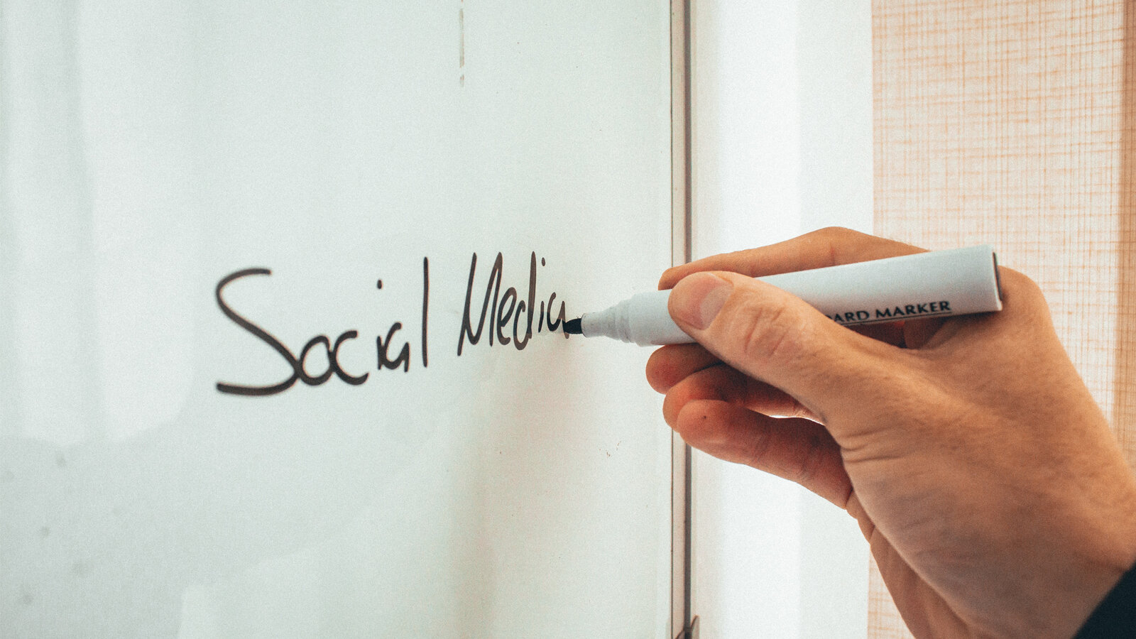 A hand holds a marker an writes Social Media on a white board.