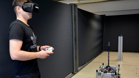 Ein junger Mann trägt eine VR-Brille und steuert einen Roboter. 