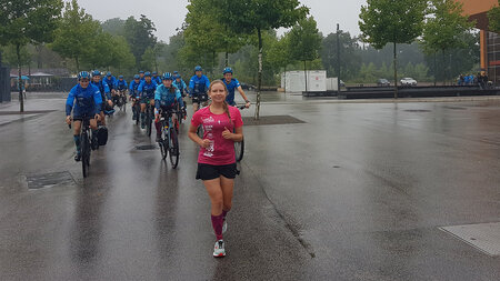 A woman is running across a rain-soaked square. Cyclists are riding along.