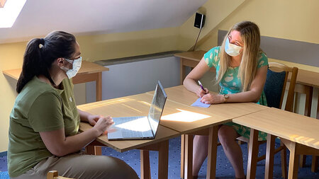 Two woman sitting against each other an wear masks.