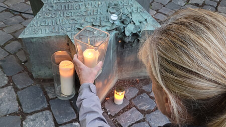 Eine Frau stellt eine Kerze neben einen Gedenkstein.