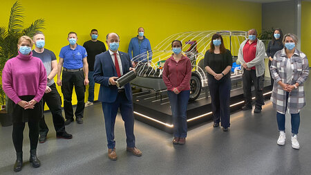Several people wearing masks stand in front of a glass car demonstrator.