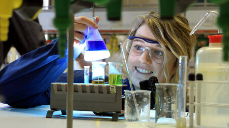 Eine Schülerin hält in einem Labor ein Reagenzglas in den Händen.