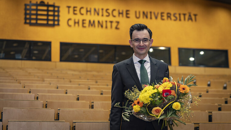 Man with a bouquet of flowers stands in a lecture hall.