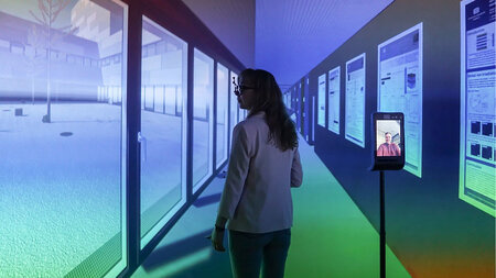 A young woman walks through a projected environment. To her right is a Double3 Telepresence robot.