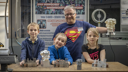 Ein Mann und drei Kinder zeigen verschiedene Metall-Bauteile, die hergestellt wurden.