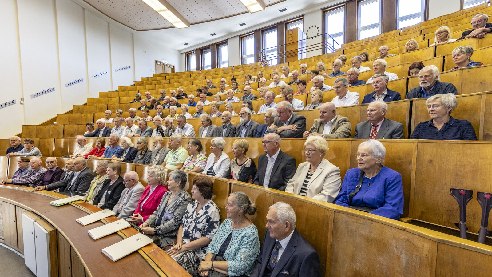 Mehrere ältere Personen sitzen in einem Hörsaal.