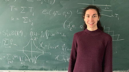 A young woman standing in front of a blackboard.