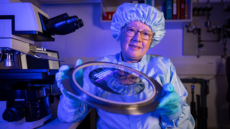 Eine Frau in Reinraumkleidung hält in einem Forschungslabor einen Wafer in der Hand.