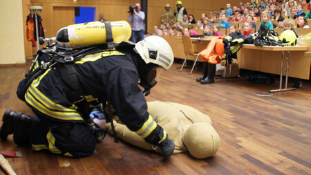 Ein Feuerwehrmann beugt sich im vollbesetzten Hörsaal über eine Puppe.
