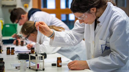 Mehrere Schüler in weißen Kitteln experimentieren im Chemielabor.