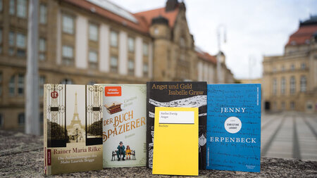 Fünf Bücher stehen auf einer Mauer vor einem Gebäude.