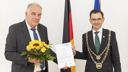 Zwei Personen stehen nebeneinander und halten eine Urkunde in den Händen.