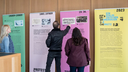 Drei Personen schauen sich Ausstellungstafeln an.