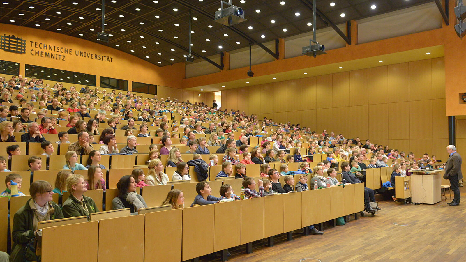 Ein Mann steht vor einem vollbesetzten Hörsaal.