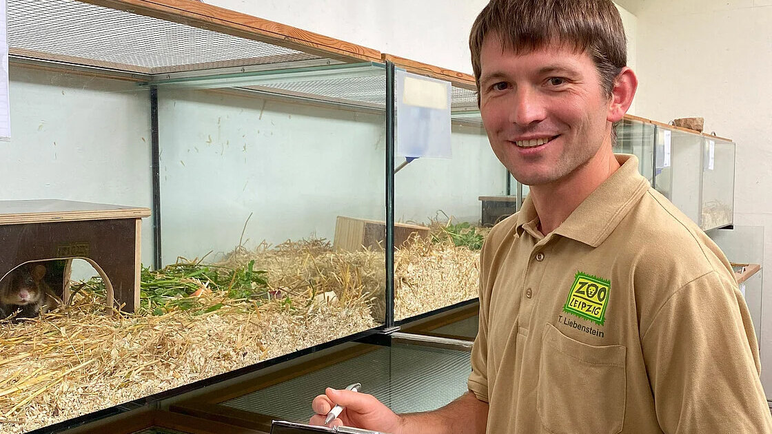 Ein Mann steht vor einem Hamstergehege.