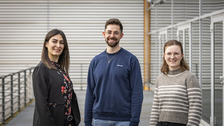 Ein Mann und zwei Frauen stehen neben einer Glasfassade.