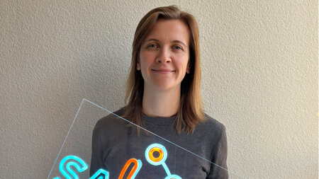 Eine Frau hält eine beleuchtete Werbetafel mit Schriftzug in den Händen.